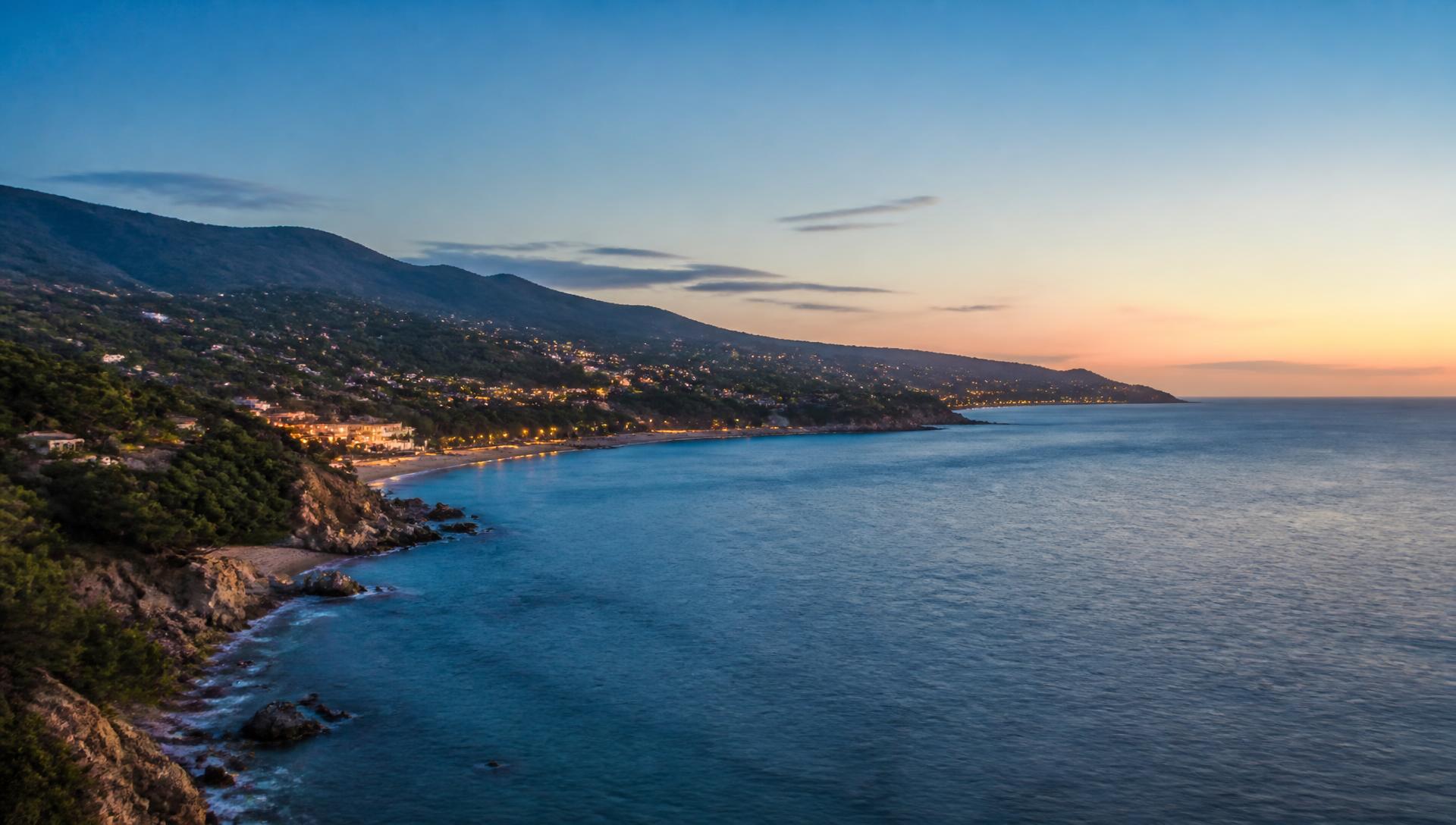 Costa del Maresme al anochecer, con el mar en calma y las luces de un pueblo costero