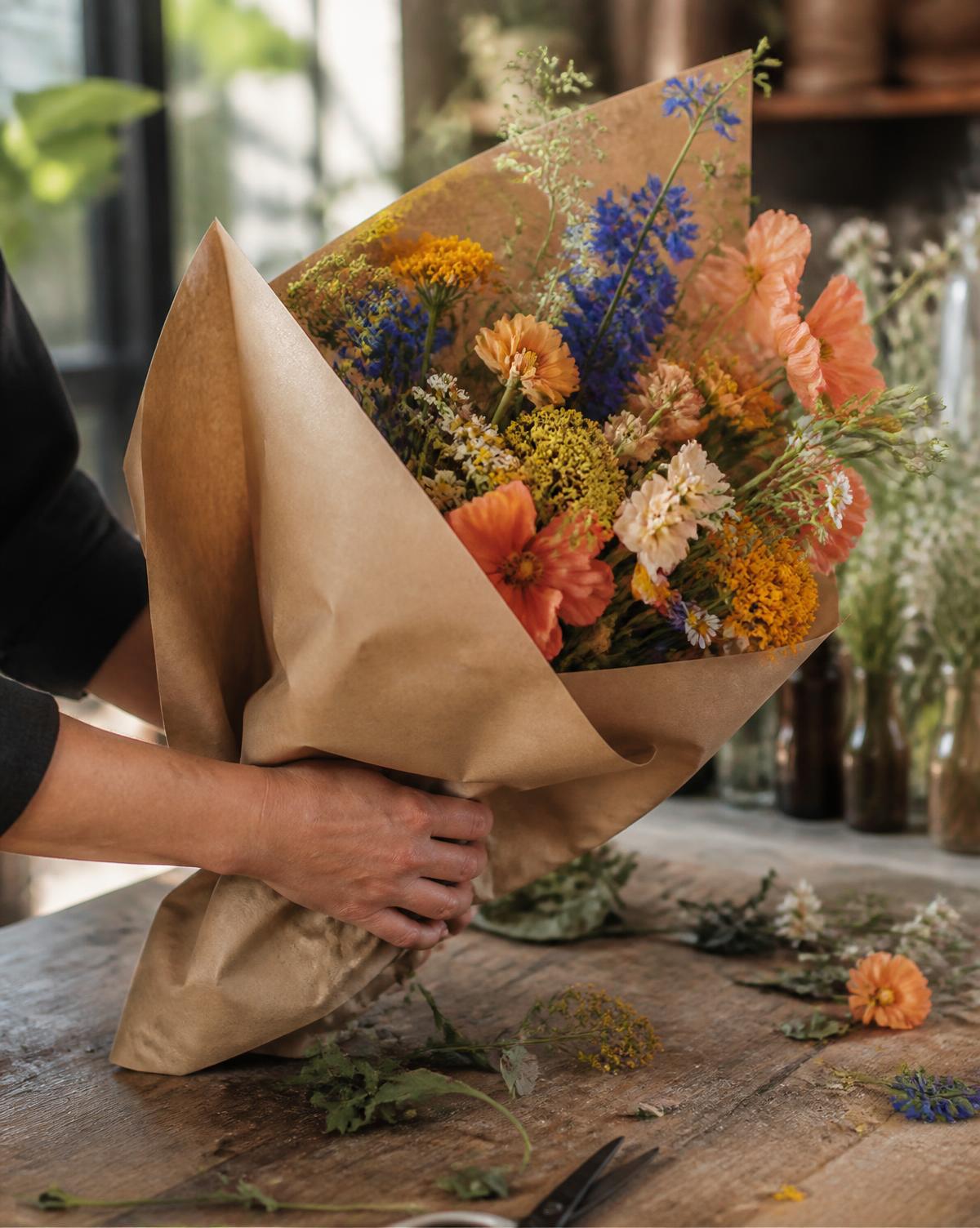 Manos envolviendo un ramo de flores de temporada en el taller de FLORA