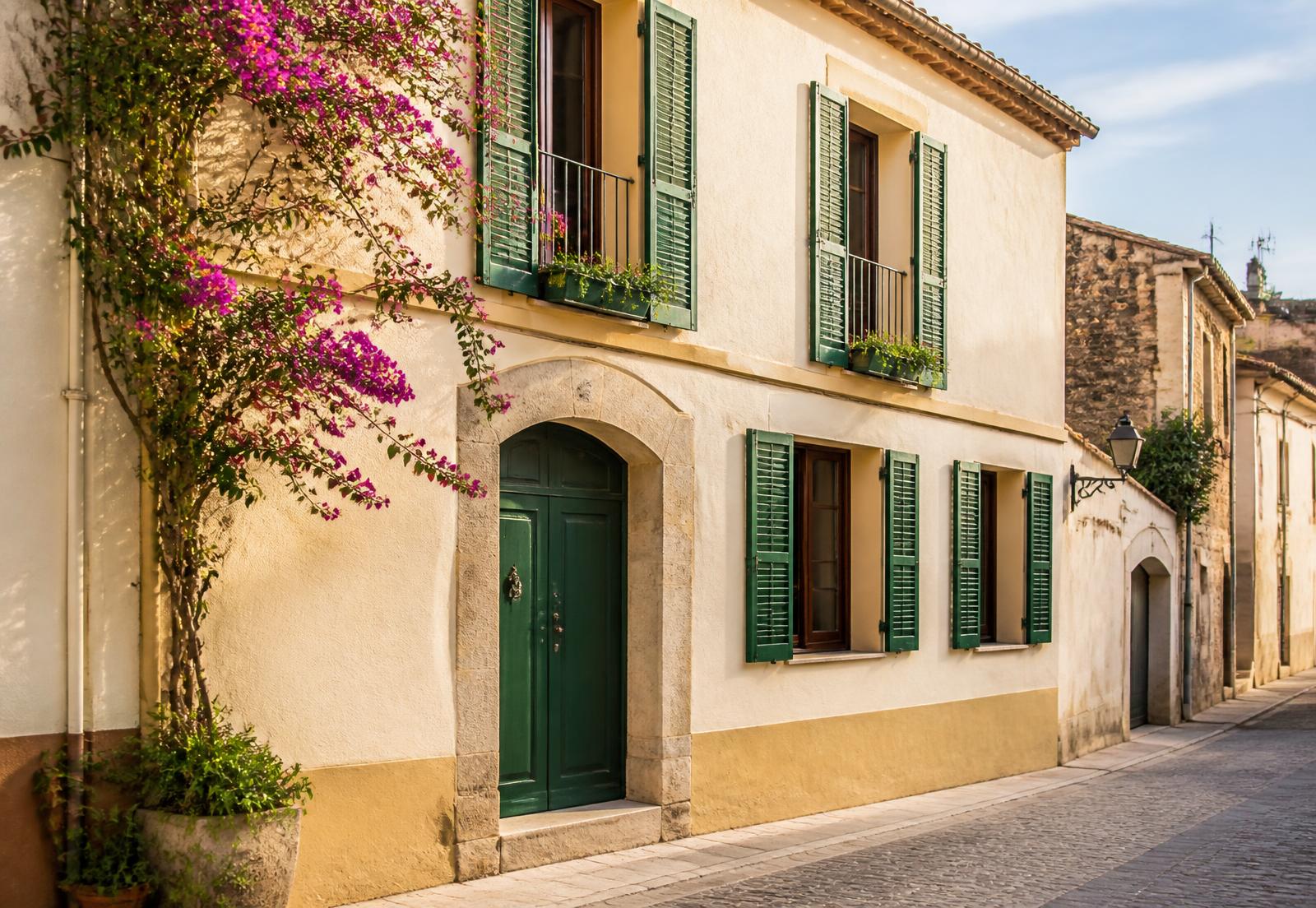 Fachada de la casa de pueblo de Premià con contraventanas verdes y buganvilla